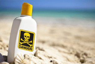 A red danger sign showing the toxic sunscreen recall warning on a sunny beach