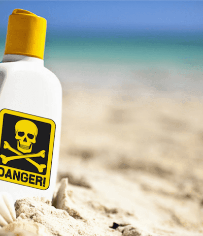A red danger sign showing the toxic sunscreen recall warning on a sunny beach
